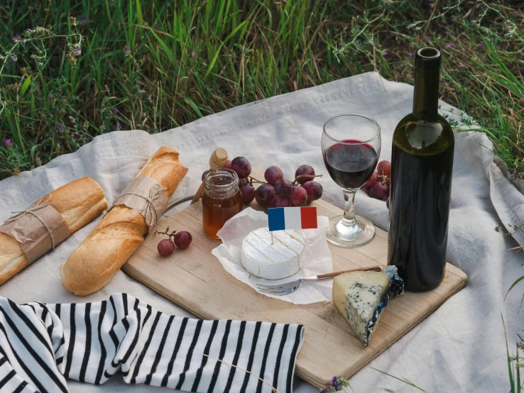 a bottle of wine sitting on top of a wooden cutting board, pexels contest winner, picnic, french flag, eating a cheese platter, dark blue and white robes