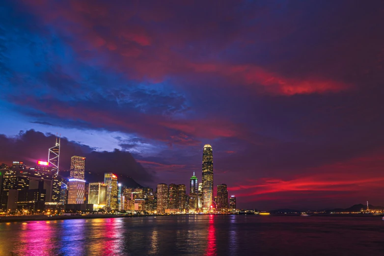 the city skyline is lit up at night, by Patrick Ching, pexels contest winner, romanticism, glowing nacreous clouds, red and blue back light, shoreline, jim cheung