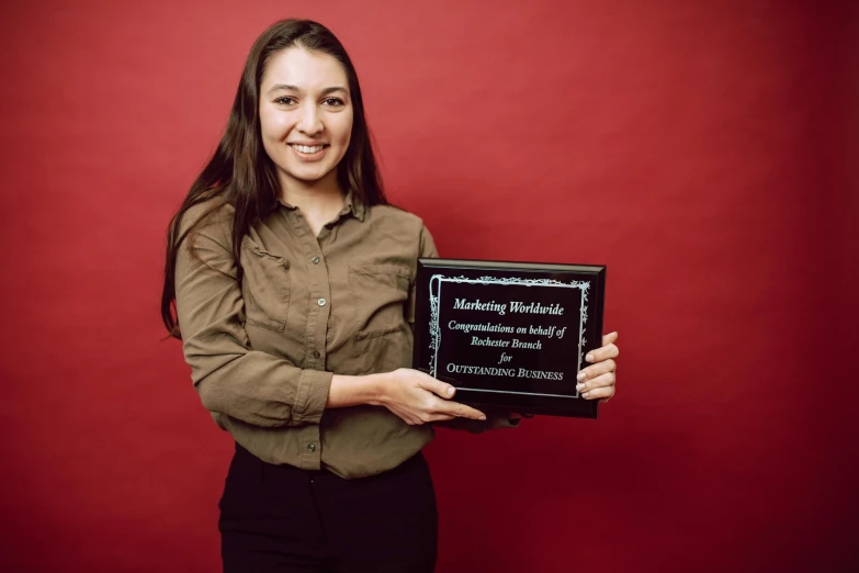 a woman holding a plaque in front of a red wall, shutterstock contest winner, vp of marketing, standing with a black background, student, andrew gonzalez