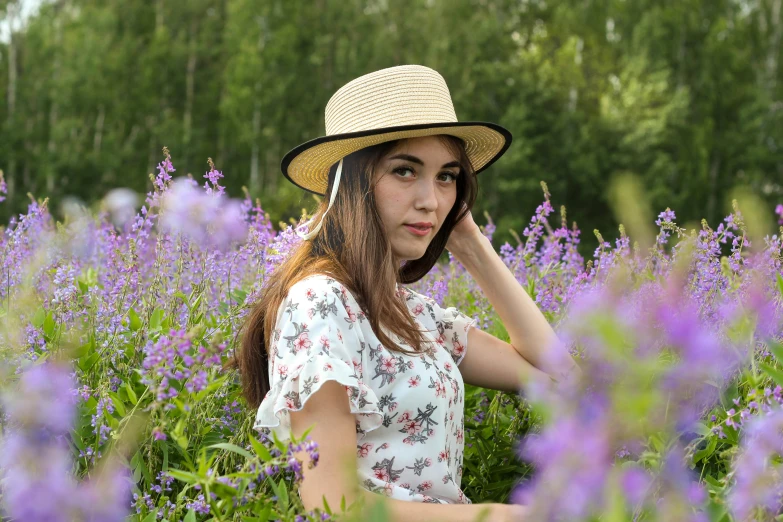 a woman sitting in a field of purple flowers, inspired by Lilia Alvarado, pexels, beige fedora, avatar image, front portrait, nordic summer