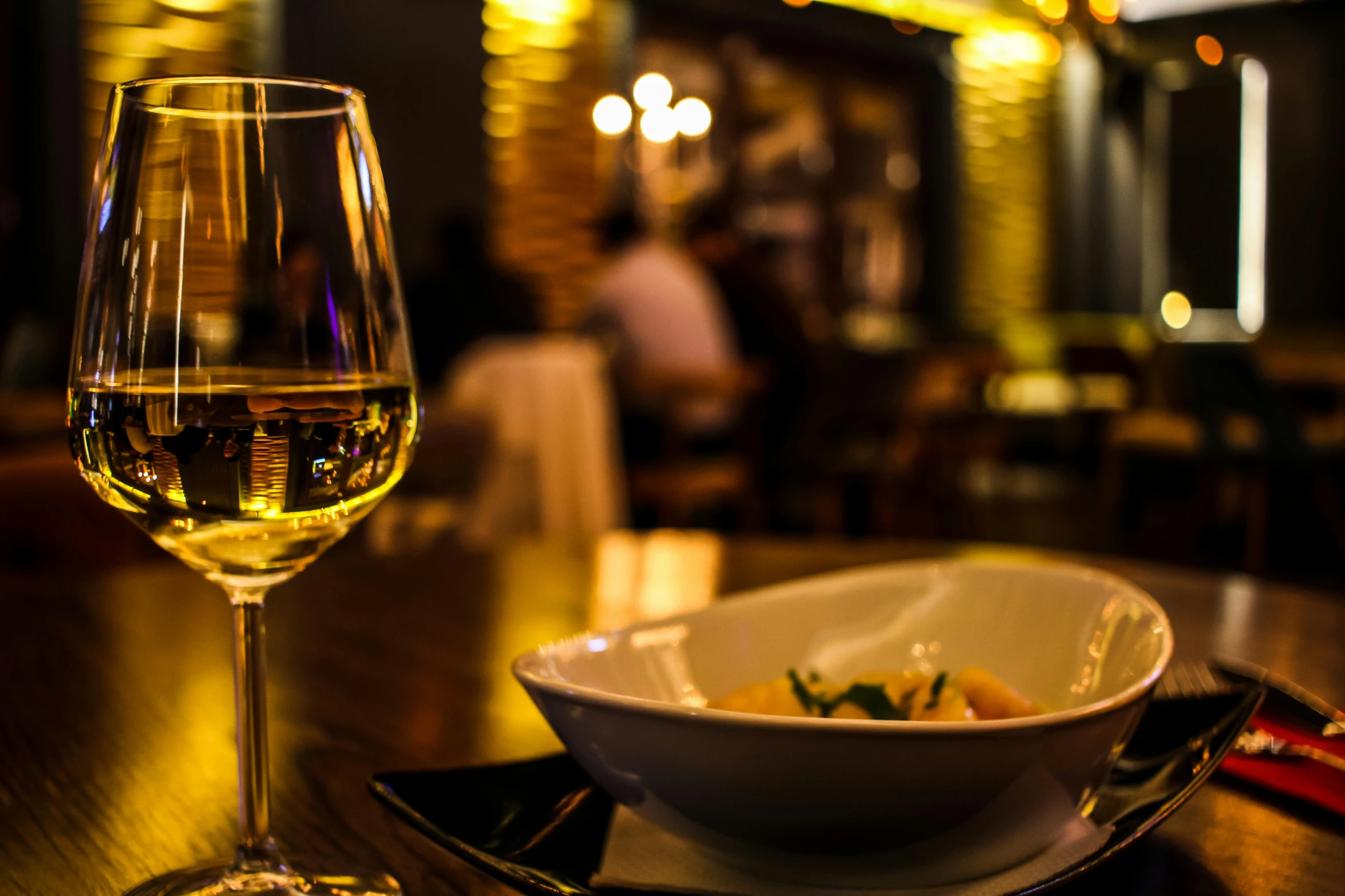 a glass of wine sitting on top of a wooden table, by Niko Henrichon, pexels contest winner, renaissance, bowl filled with food, sitting at a bar, golden glow, place setting