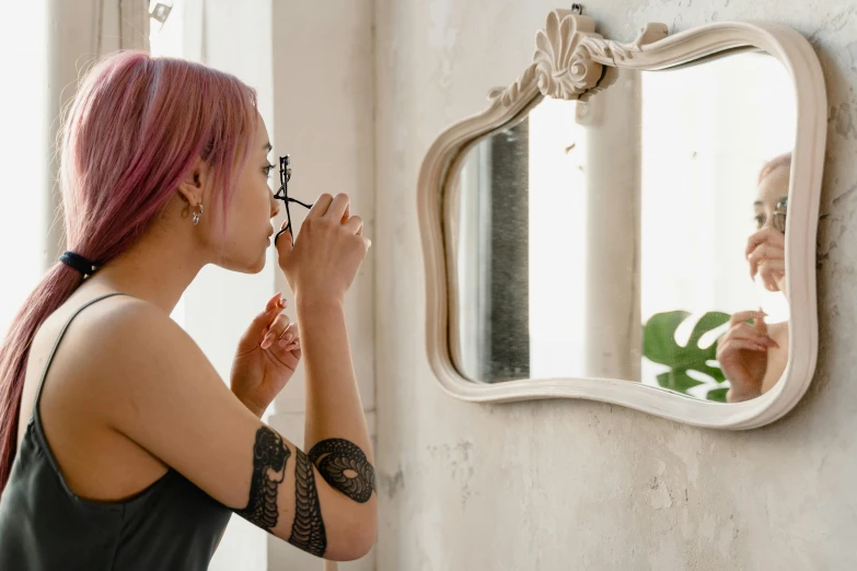 a woman brushing her teeth in front of a mirror, inspired by Elsa Bleda, trending on pexels, aestheticism, with a tentacle tattoo, woman with rose tinted glasses, profile image, small square glasses