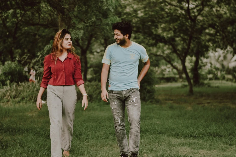 a man and a woman walking in the grass, wondering about others, background image, trees in the background, wearing pants and a t-shirt