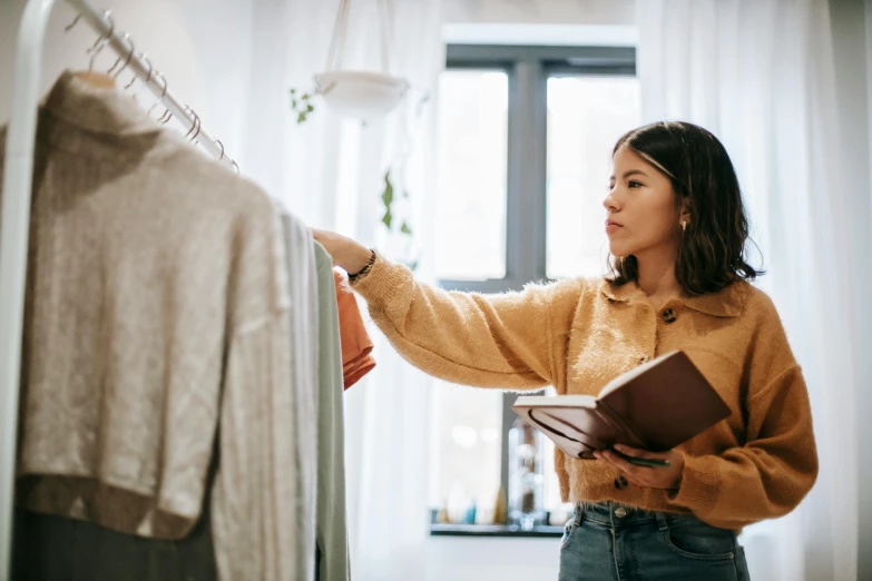 a woman looking at clothes on a hanger, trending on pexels, holding spell book, thumbnail, inspect in inventory image, looking away