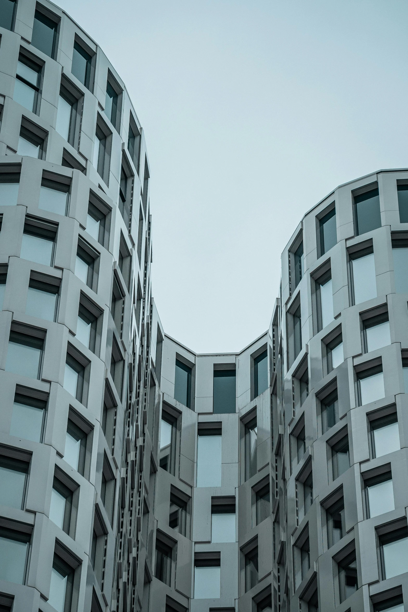 a couple of tall buildings sitting next to each other, a photo, unsplash contest winner, modernism, flat grey color, curved body, convoluted halls, broken buildings