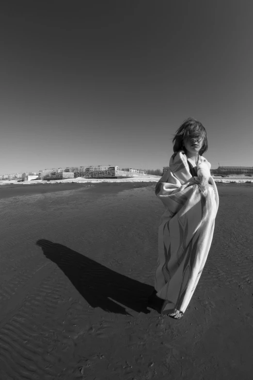 a woman standing on top of a sandy beach, a black and white photo, surrealism, wearing white silk robe, 15081959 21121991 01012000 4k, portrait casting long shadows, wearing! robes!! of silver