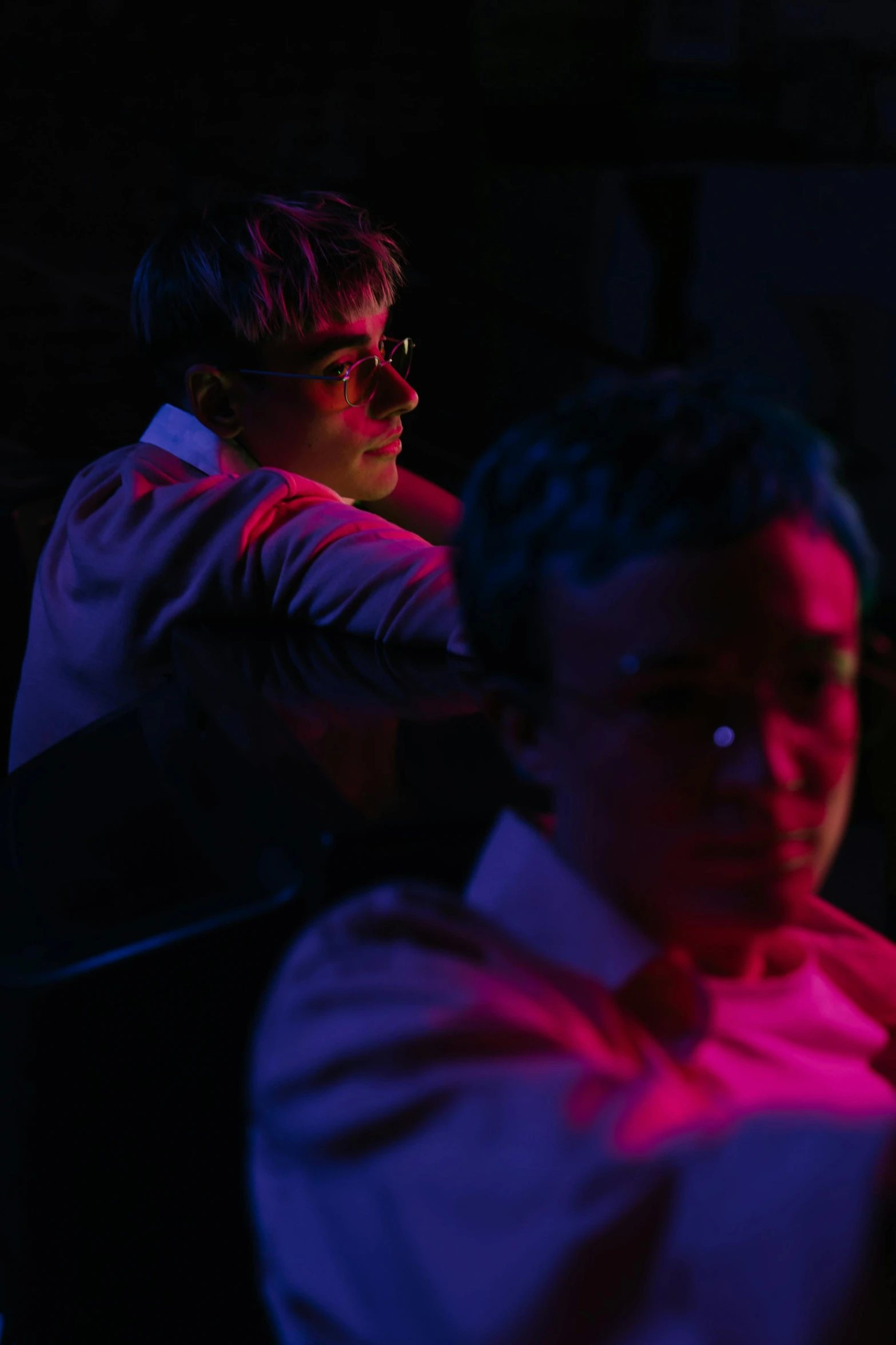 a couple of men sitting next to each other, an album cover, by David Donaldson, unsplash, serial art, dim red light, julian ope, movie scene close up, looking from shoulder