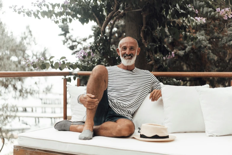 a man sitting on top of a white couch, a portrait, inspired by Jean-Yves Couliou, pexels contest winner, grey trimmed beard, happy italian beach scene, wearing stripe shirt, balcony