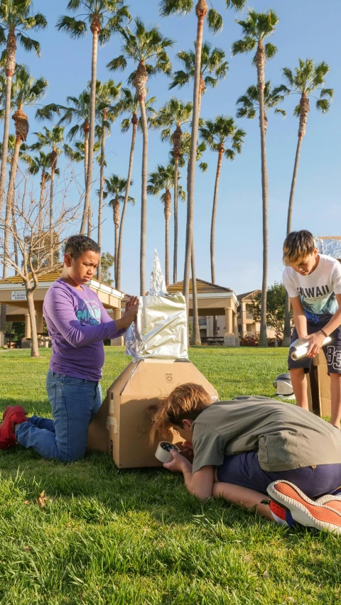 a group of people standing on top of a lush green field, robot made of a cardboard box, rocket launch, oceanside, at a park