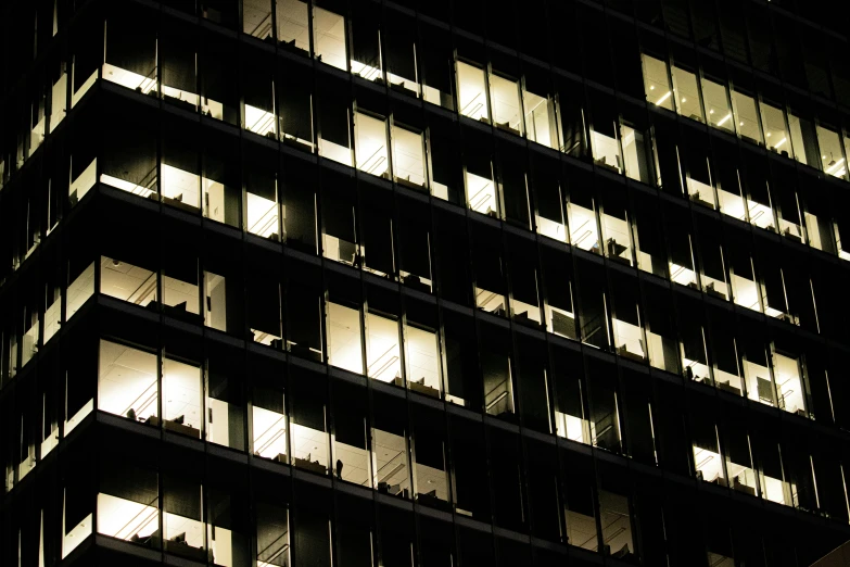 a tall building with lots of windows lit up at night, a photo, inspired by Andreas Gursky, pexels, office cubicles, black windows, people at work, afternoon