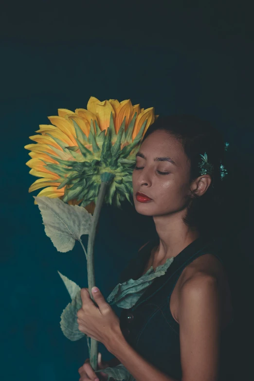 a woman holding a sunflower in front of her face, an album cover, inspired by Elsa Bleda, hyperrealism, asian women, profile image, standing with a black background, portrait of vanessa morgan