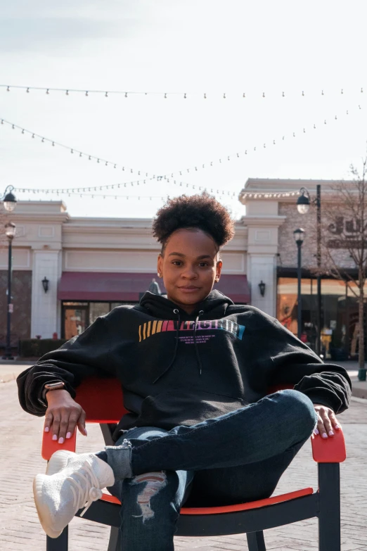 a young man sitting on top of a red chair, featured on instagram, black arts movement, at a mall, an epic non - binary model, in a hoodie, upon a peak in darien