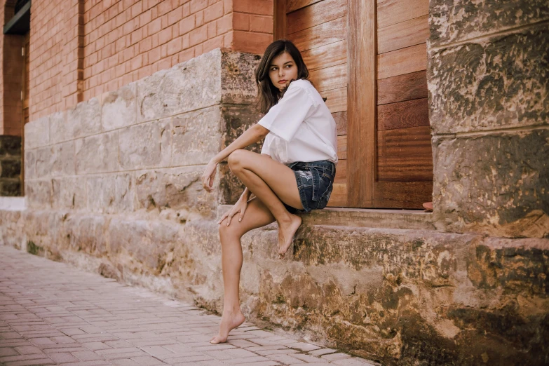 a woman sitting on the side of a brick building, pexels contest winner, hyperrealism, tan skin a tee shirt and shorts, beautiful mexican woman, hairy legs, white clothes