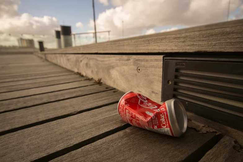 a can of coke sitting on top of a wooden bench, by Jacob Toorenvliet, ((unreal engine)), the thames is dry, trash can, high winds