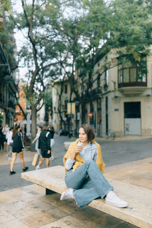 a woman sitting on top of a wooden bench, trending on unsplash, happening, gothic quarter, yellow clothes, eating outside, university