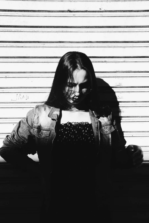 a woman standing in front of a garage door, a black and white photo, aphex twin, christina ricci, denim, the girl and the sun