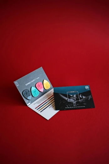 two business cards sitting next to each other on a red surface, a picture, color field, black and teal paper, modelling clay, epk, detailed product image