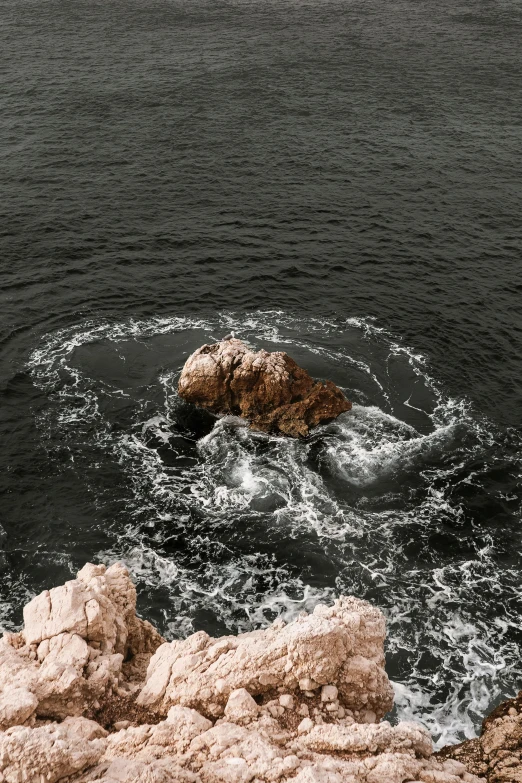 a large body of water next to a rocky shore, pexels contest winner, romanticism, whirlpool, desaturated color, mediterranean, drops around