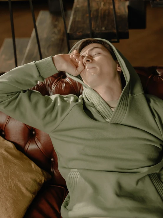 a man that is laying down on a couch, a colorized photo, inspired by Elsa Bleda, trending on unsplash, renaissance, in a hoodie, sage green, facepalm, robe. perfect face