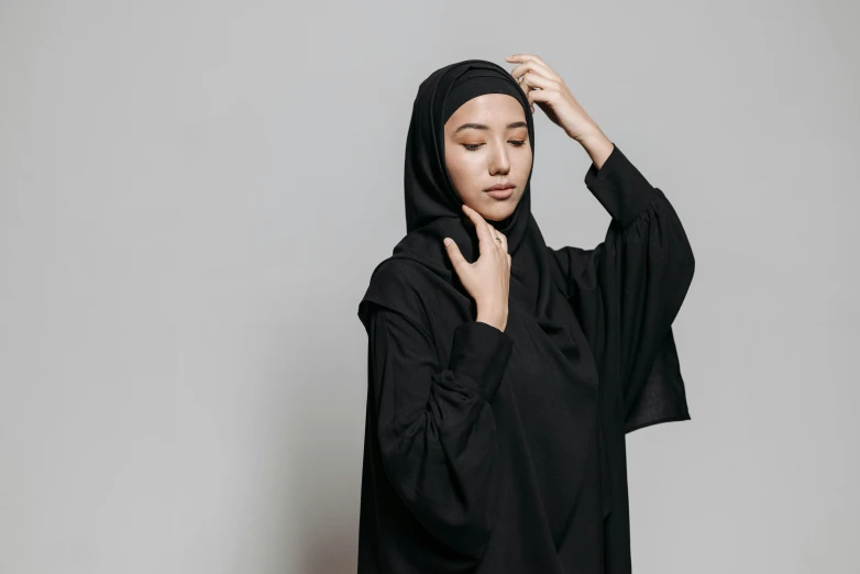 a woman wearing a black hijab, inspired by Modest Urgell, pexels contest winner, hurufiyya, on a gray background, young asian woman, religious robes, woman in streetwear