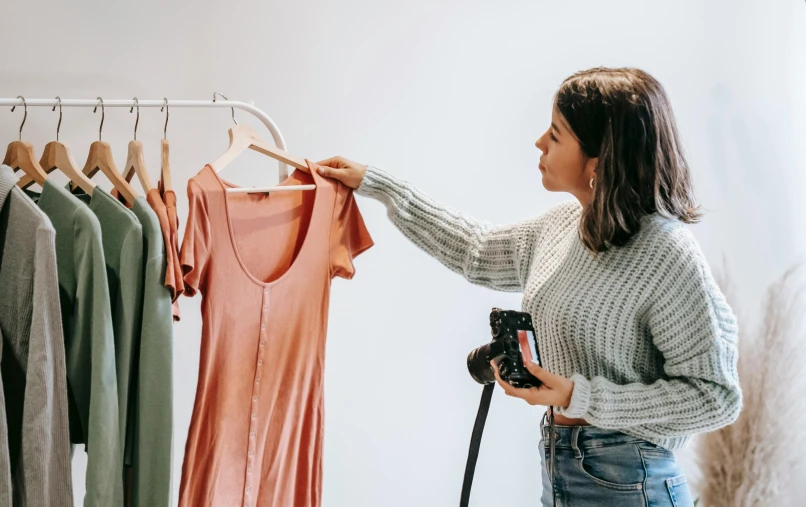 a woman standing in front of a rack of clothes, holding a camera, inspect in inventory image, pokimane, wearing a designer top