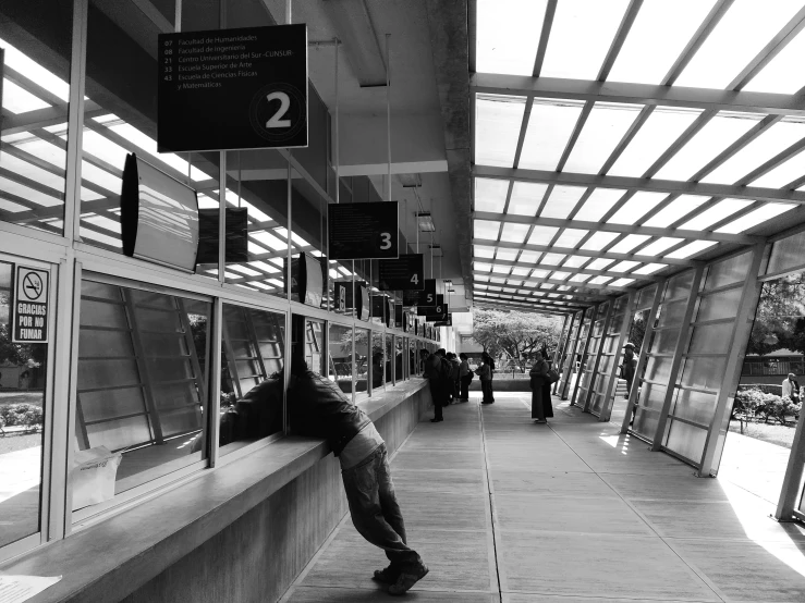 a black and white photo of a person leaning against a window, a black and white photo, flickr, happening, monorail station, benches, floor b2, in line