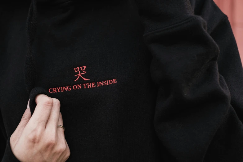 a person wearing a black hoodie with the words crying on the inside, inspired by Yu Zhiding, trending on pexels, sōsaku hanga, embroidered shirt, crimson themed, inside, gemma chen