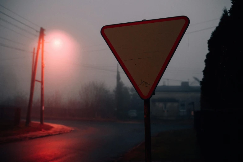 a street sign sitting on the side of a road, by Adam Marczyński, pexels contest winner, red illuminating fog, triangle, simin stalenhag, very hazy