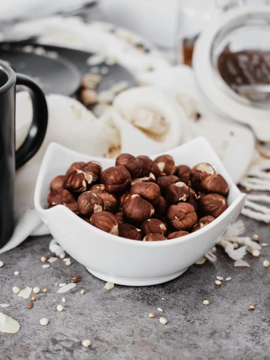 a white bowl filled with nuts next to a cup of coffee, inspired by Károly Patkó, unsplash, coconuts, close-up product photo, fully chocolate, hasbulla