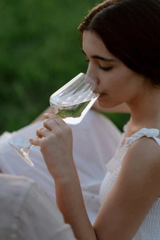 a woman in a white dress drinking a glass of wine, inspired by Konstantin Somov, unsplash, peacefully drinking river water, exterior shot, soft evening lighting, award - winning details