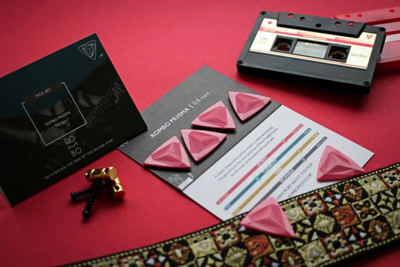 a close up of some items on a table, an album cover, video art, covered with pink marzipan, intricate triangular designs, invitation card, black and red scheme