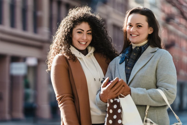 two women standing next to each other on a city street, trending on pexels, renaissance, brown clothes, people shopping, promotional image, smiling slightly