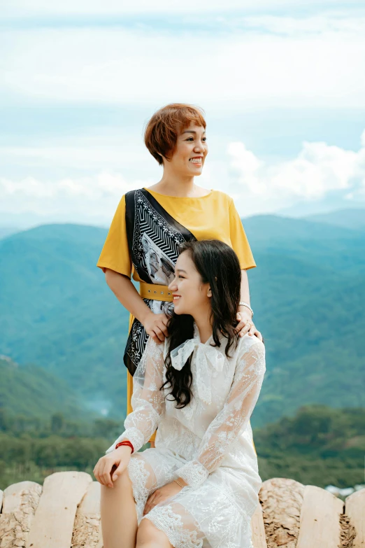 a couple of women sitting on top of a stone wall, a picture, by Tan Ting-pho, pexels contest winner, dau-al-set, with short hair, promotional image, mountainous, yellow