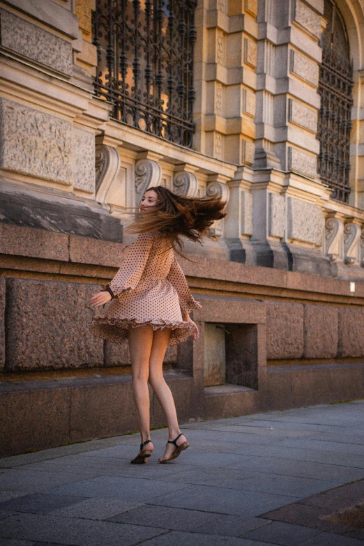 a woman walking down a sidewalk next to a building, pexels contest winner, arabesque, long hair windy, prima ballerina, saint petersburg, jumping