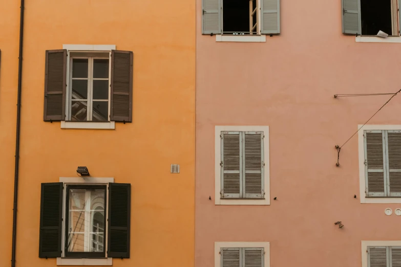 a bird sitting on a window sill in front of a building, inspired by Wes Anderson, pexels contest winner, renaissance, orange pastel colors, house windows, 3 colours, metallic shutter