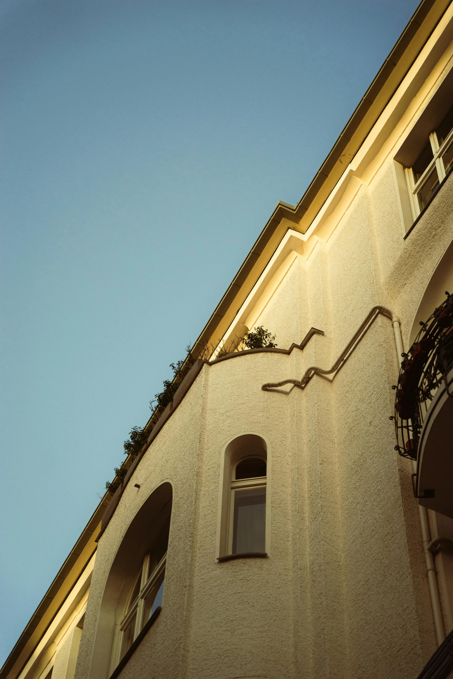 a clock that is on the side of a building, a photo, inspired by Ricardo Bofill, unsplash, art nouveau, soft golden light, roof with vegetation, low - angle shot from behind, pale yellow walls