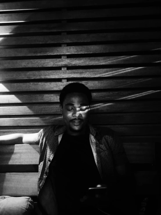 a black and white photo of a man sitting on a bench, inspired by Gordon Parks, unsplash, light and space, selfie!!!!! of a man, childish gambino, glowing light and shadows, sitting in a cafe