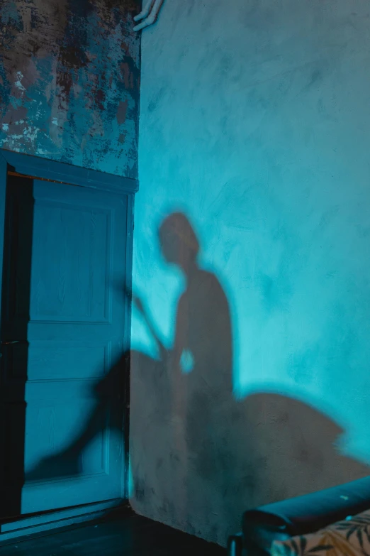 a shadow of a person on a wall next to a bed, by Elsa Bleda, pexels contest winner, conceptual art, blue colored, leaning on door, film still of batman, ( ( theatrical ) )