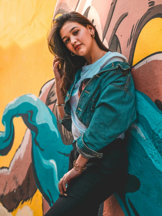 a woman leaning against a graffiti covered wall, trending on pexels, with teal clothes, avatar image, wearing a jeans jackets, portrait image