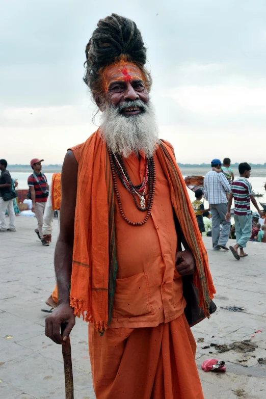 a man standing on top of a sandy beach, inspired by Bapu, hairy orange body, diverse costumes, wise old man, taken in the late 2010s