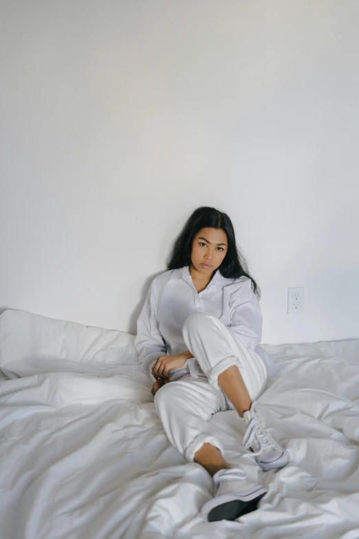 a woman sitting on top of a white bed, inspired by Elsa Bleda, trending on pexels, white uniform, charli xcx, androgynous male, multiple stories