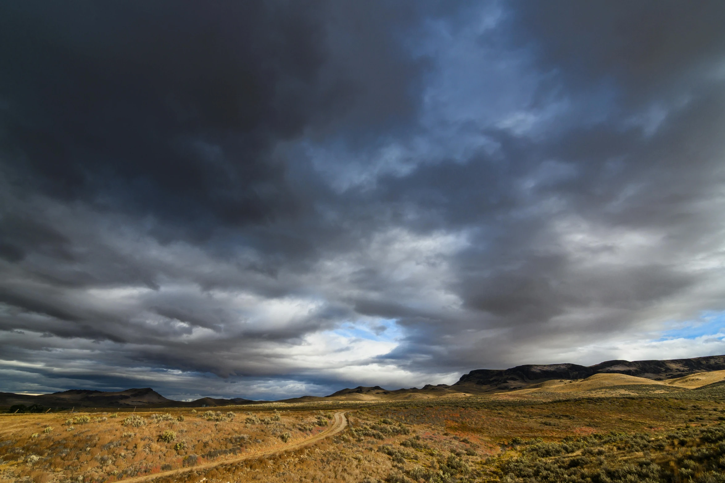 a dirt road running through a field under a cloudy sky, by Peter Churcher, wind river valley, large scale photo, dramatic lightin, today\'s featured photograph 4k