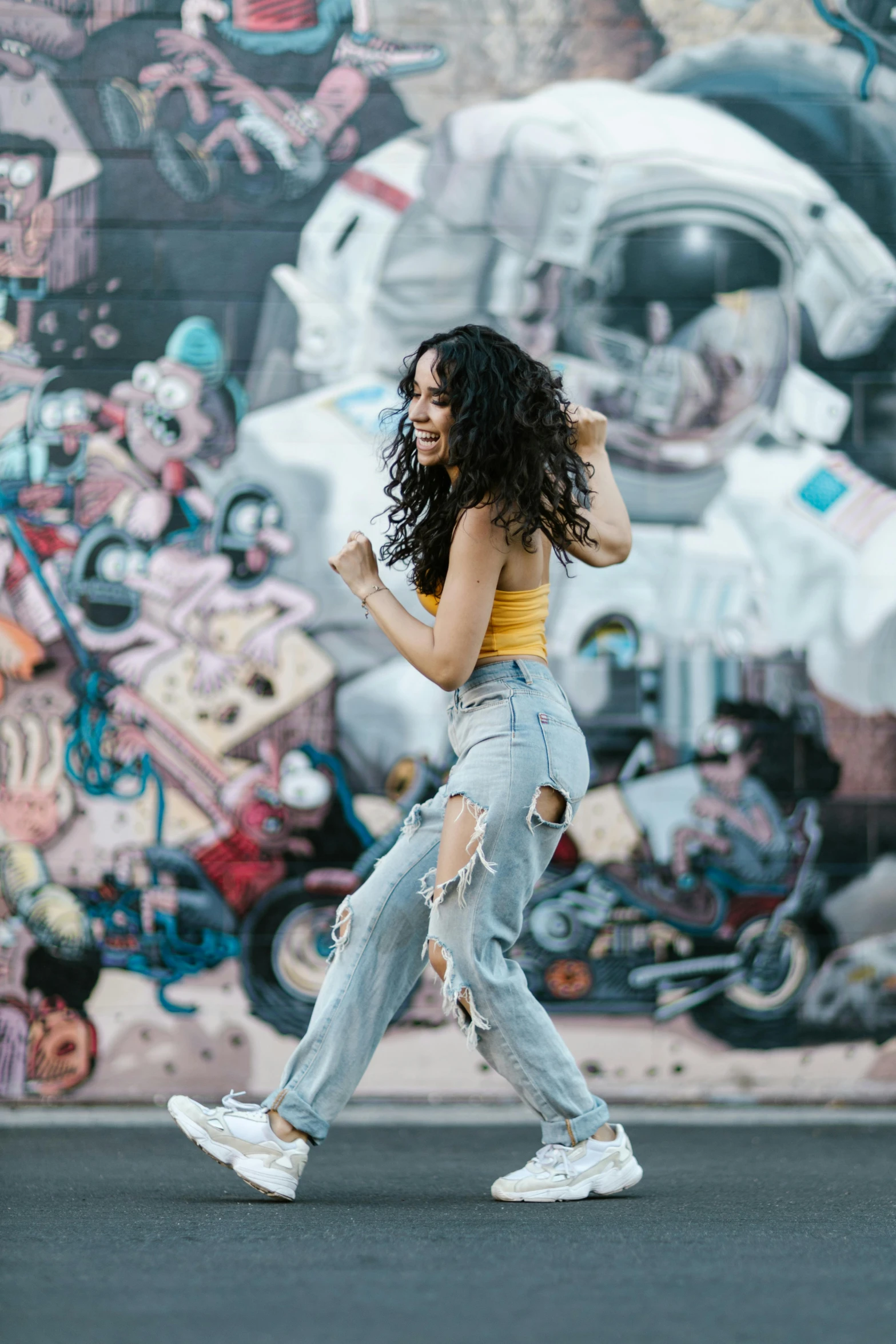 a woman dancing in front of a graffiti wall, trending on pexels, portrait of vanessa morgan, ripped jeans, oona chaplin, wearing yellow croptop