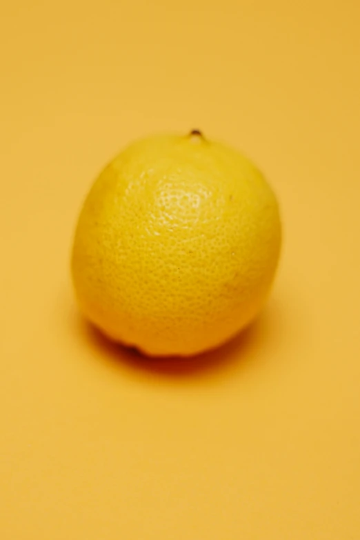 a close up of a lemon on a yellow background, a stipple, trending on unsplash, minimalism, shot on sony alpha dslr-a300, standing, orange: 0.5, plump