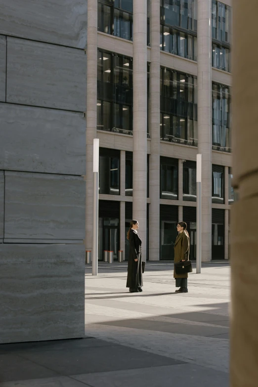 a man riding a skateboard down a sidewalk next to a tall building, inspired by David Chipperfield, face to face staring, ready for a meeting, large pillars, man and woman walking together