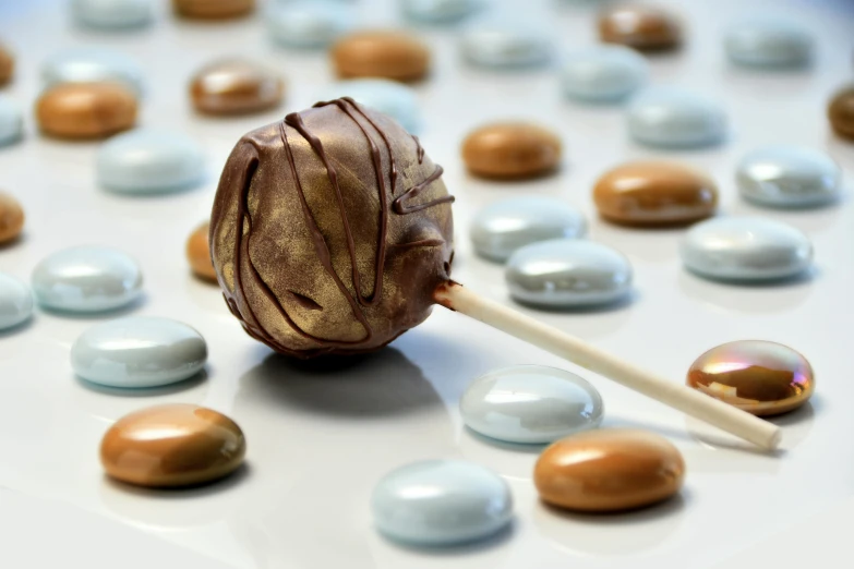 a chocolate lollipop sitting on top of a table, inspired by Joris van der Haagen, shutterstock contest winner, light grey blue and golden, candy treatments, made of liquid metal and marble, thumbnail