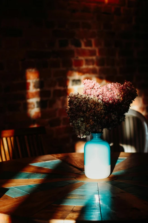 a vase of flowers sitting on top of a wooden table, unsplash, light and space, dimly lit cozy tavern, pale blue backlight, vivid and vibrant, mid morning lighting