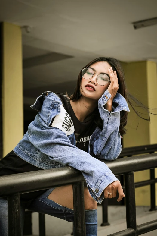 a woman with glasses sitting on a railing, by Robbie Trevino, trending on pexels, realism, denim jacket, asian face, bella poarch, 15081959 21121991 01012000 4k