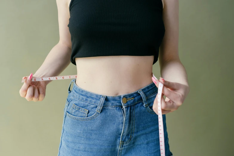 a woman measuring her waist with a tape, by Julia Pishtar, trending on pexels, an anthropomorphic stomach, wearing denim, wearing black shorts, wearing a tanktop and skirt