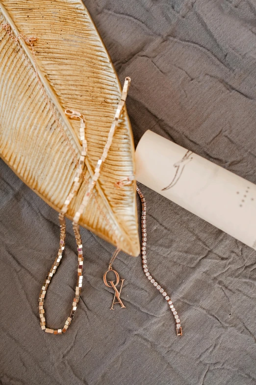 a feather laying on top of a bed next to a roll of paper, inspired by Jacopo Bellini, jewelry display, cyber copper spiral decorations, pearls and gold chains, sustainable materials